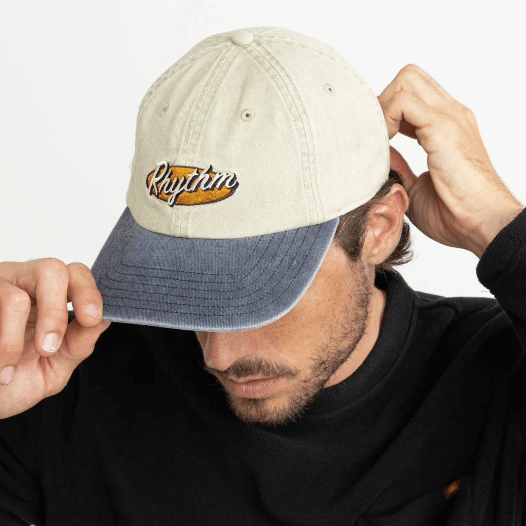 Rhythm Hallmark Cap available at Stewart’s Menswear Mullumbimby. Men’s cotton twill cap with embroidered logo and snap back. Photo of model wearing Rhythm Hallmark Cap, front view.