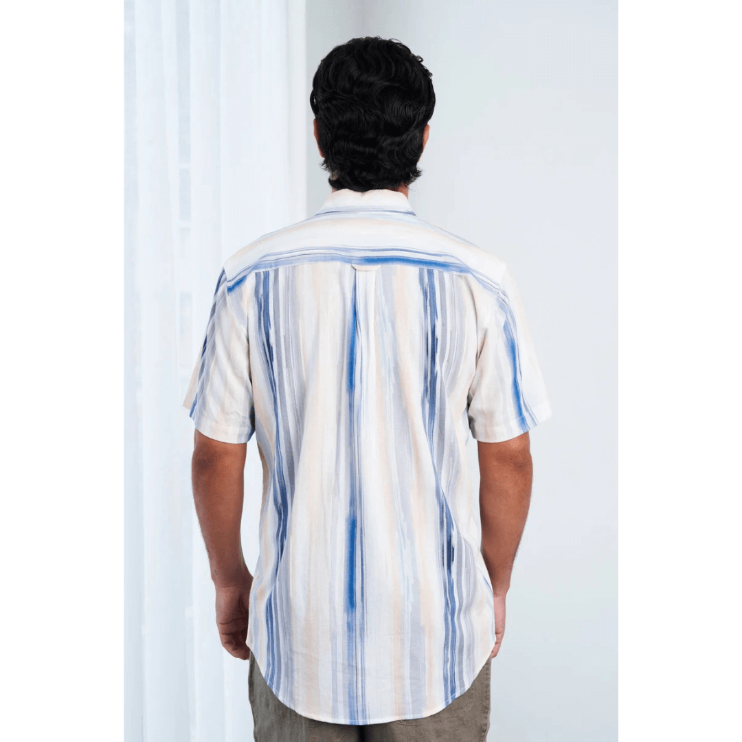Back view of model wearing men’s Hemp Rayon Waterfall Short Sleeve Shirt – Blue Peach. Soft hemp-rayon blend, available at Stewart’s Menswear Mullumbimby. White shirt with blue and peach coloured waterfall type stripes running downwards.
