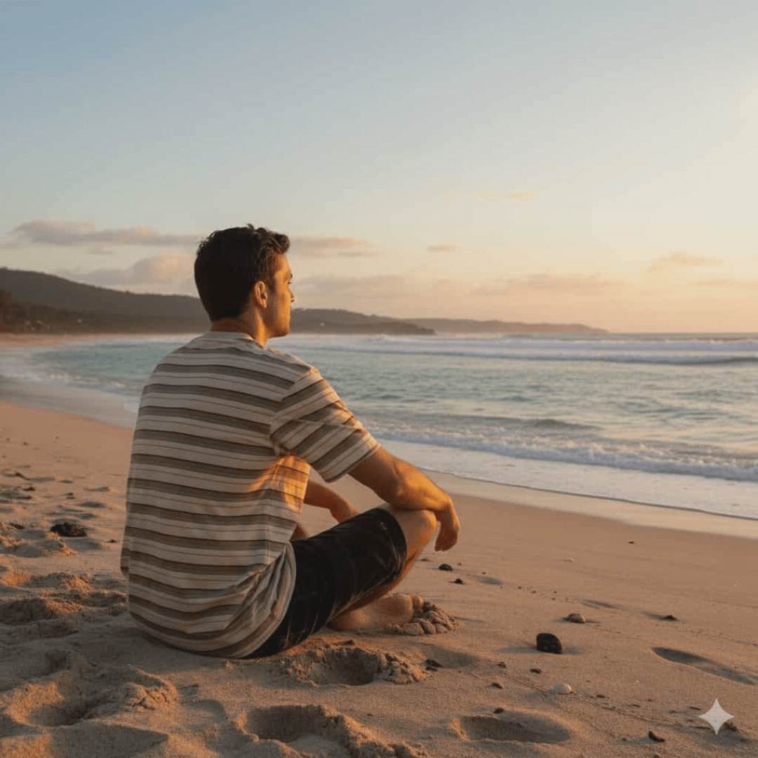 Carve Vintage Short Sleeve Tee available at Stewart’s Menswear Mullumbimby. Regular fit men’s striped cotton jersey t-shirt with chest badge. Lifestyle photo of man wearing Carve Vintage Tee sitting on a beach watching the waves.