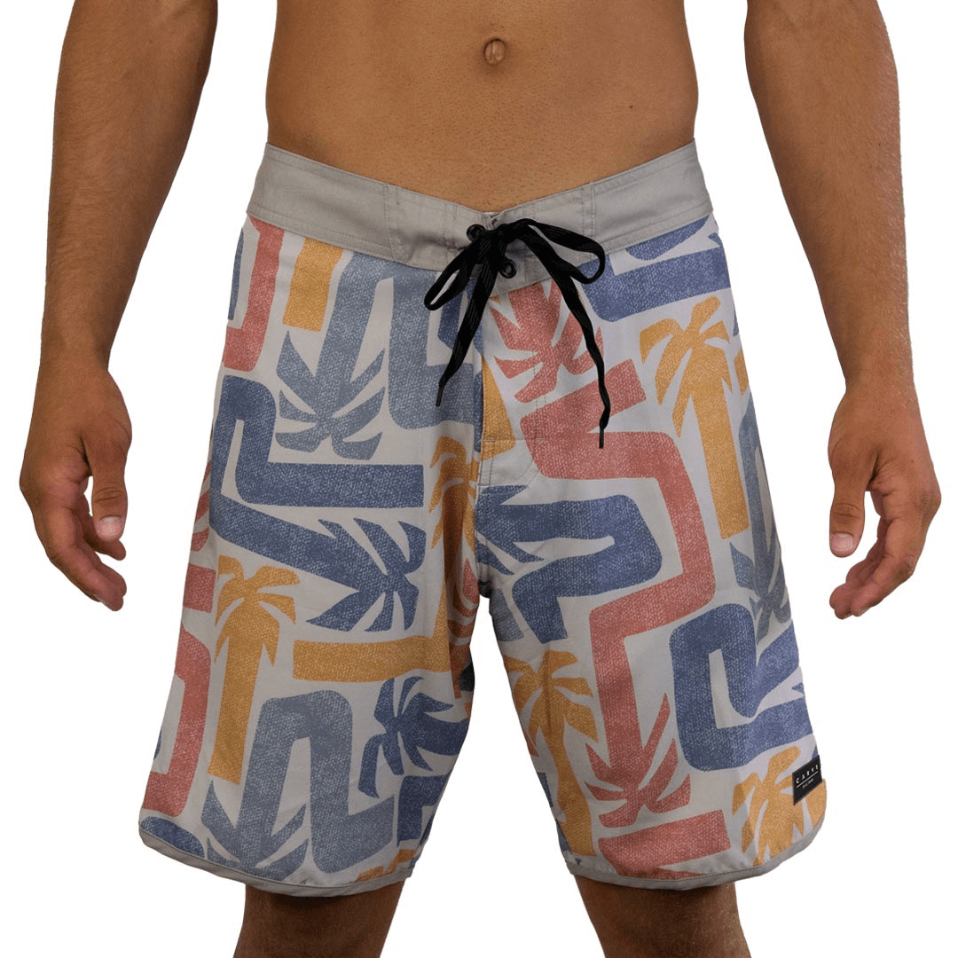 Stewarts Menswear Carve Pandanus Boardshort. Men's scoop leg boardie with fitted waistline. Front tabs and draw cord, front elastane gusset fly and 19" leg length. Concealed zip pocket at back and carve logo badge on left leg. All over sublimated print white background with abstract pandanus palms in washed red, mustard and blue colours.