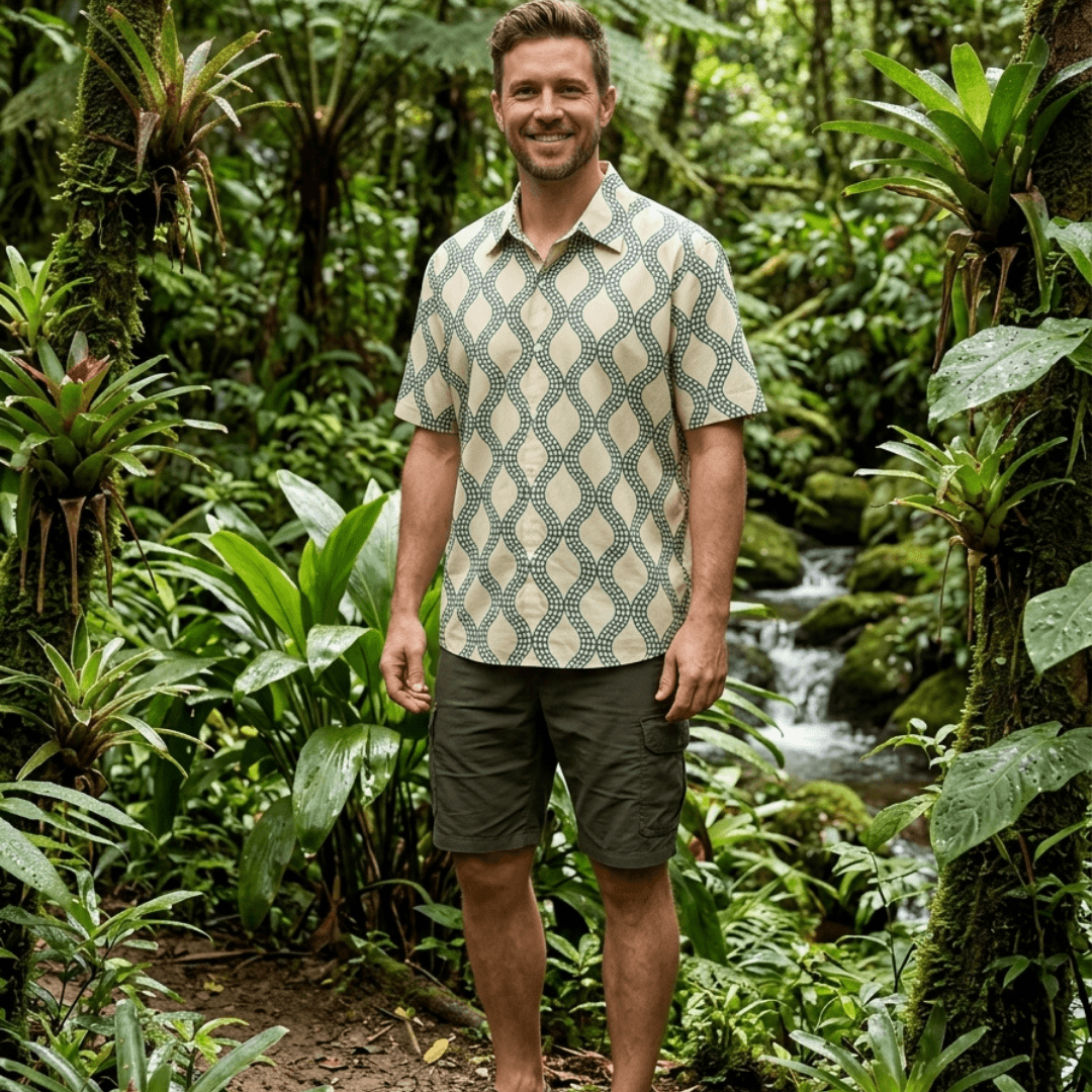 Man standing in a rainforest wearing a Cochin Blue Python Shirt in sage green wave print, hand printed cotton voile shirt available at Stewart's Menswear Mullumbimby.