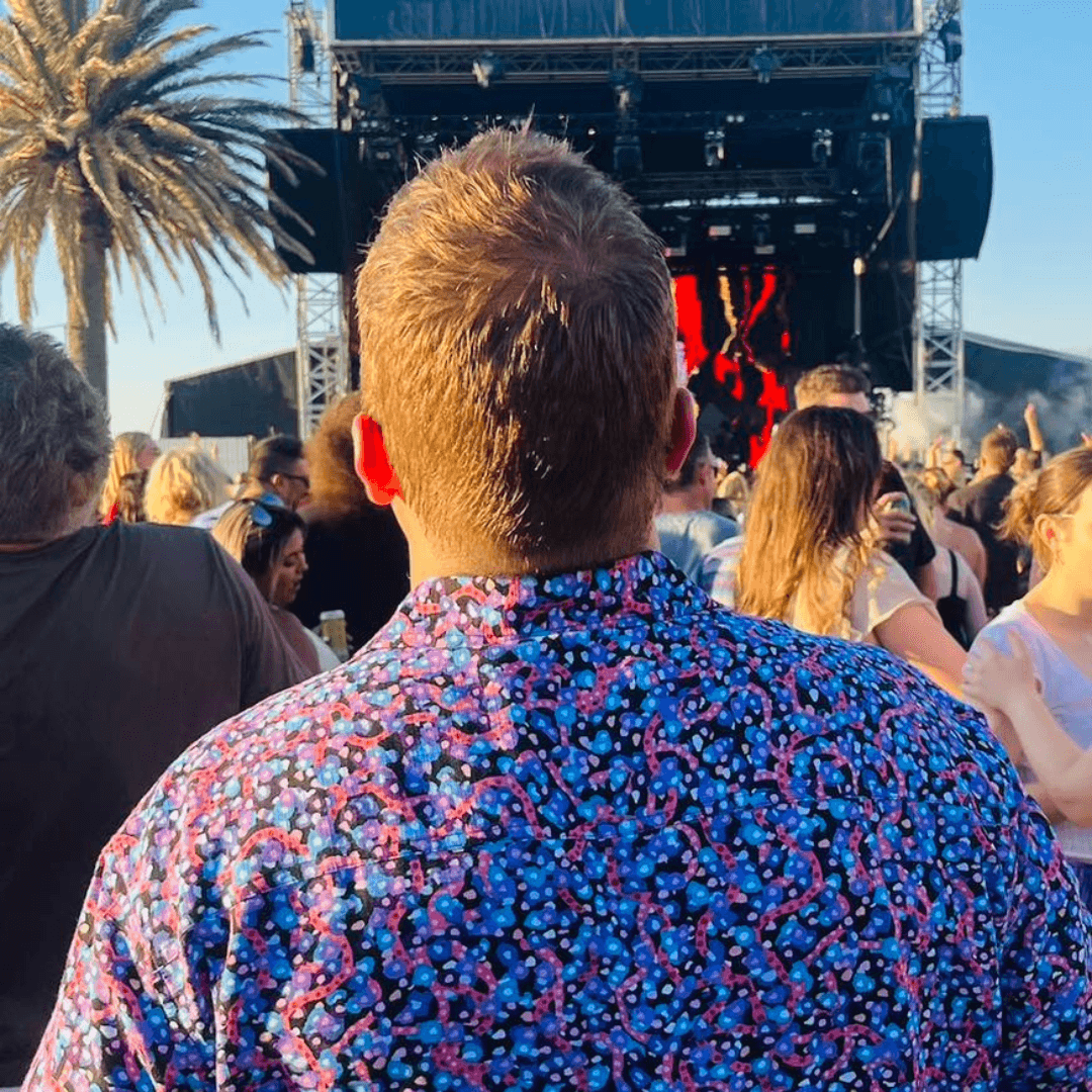 Man wearing a bright coloured shirt at an outdoor concert. Kingston Grange Bamboo Dreaming short sleeve shirt in Ngalyipi Jukurrpa pattern available at Stewart's Menswear in Mullumbimby.