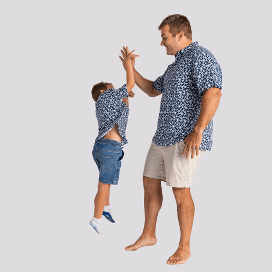Man and child wearing matching blue patterned shirts and denim shorts on a light gray background. Kingston Grange bamboo Asanoha print bamboo shirt available in Men's and Boys' sizes from Stewart's Menswear, Mullumbimby.
