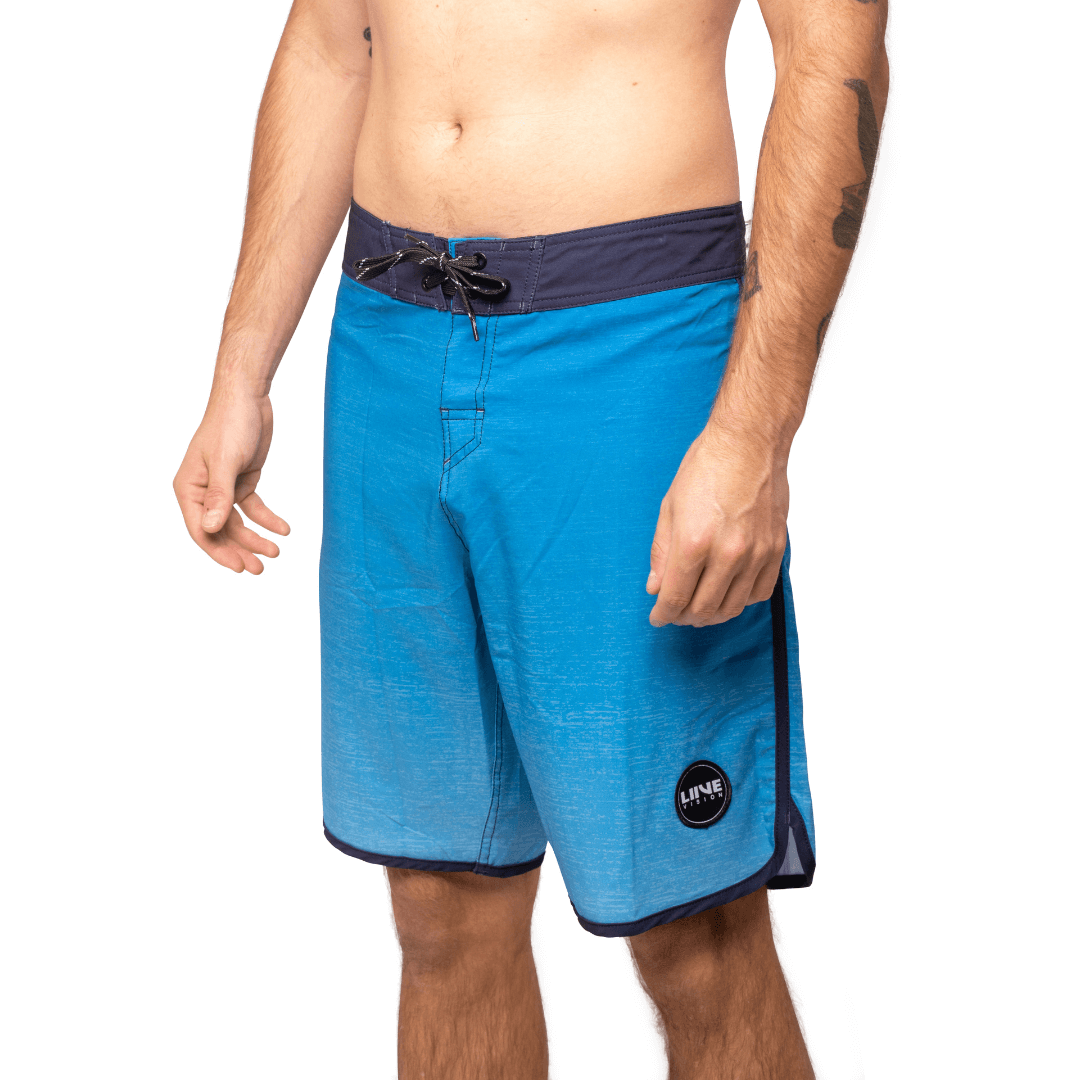 Stewarts Menswear Liive Vision Apparel Vague Boardshort. Trendy gradient colour design. Fitted waist with drawcord, back patch pocket with velcro closure and keep loop in the back pocket. Dark blue waistband with gradient blue body. Scalloped leg with navy piping. Front View.