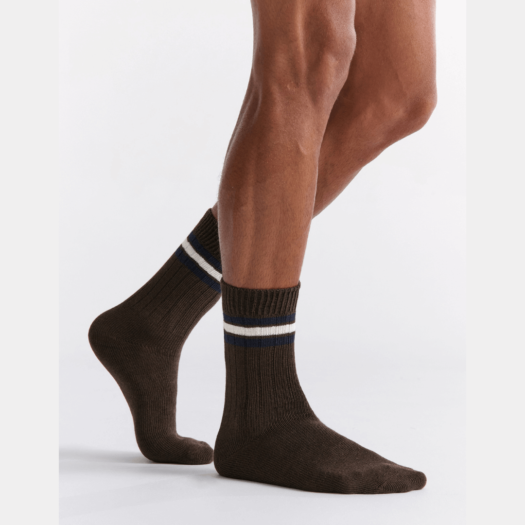 Stewarts Menswear Mullumbimby. Ambra Men's Chunky rib tennis stripe crew socks. Organic Cotton socks. Chocolate brown colour with three stripes at top (2 x Navy with 1 x white in between). Photo shows model wearing Ambra men's chunky rib tennis crew socks in Cappucino.