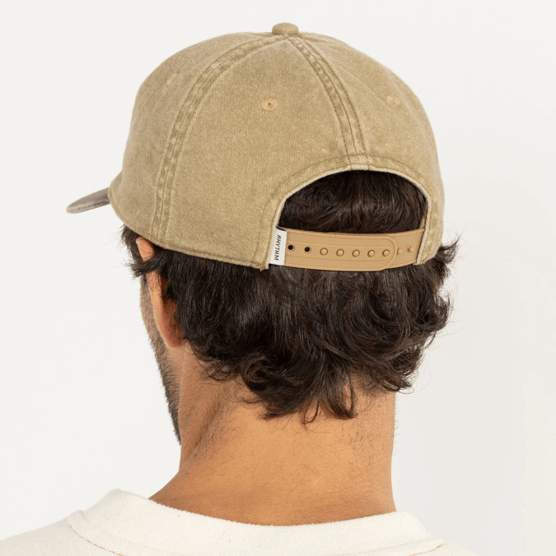 Stewart's Menswear, Mullumbimby. Rhythm Hallmark Cap. Sand coloured with embroidered Rhythm branding and darker brown coloured peak. Photo shows model wearing Hallmark Cap, back view.