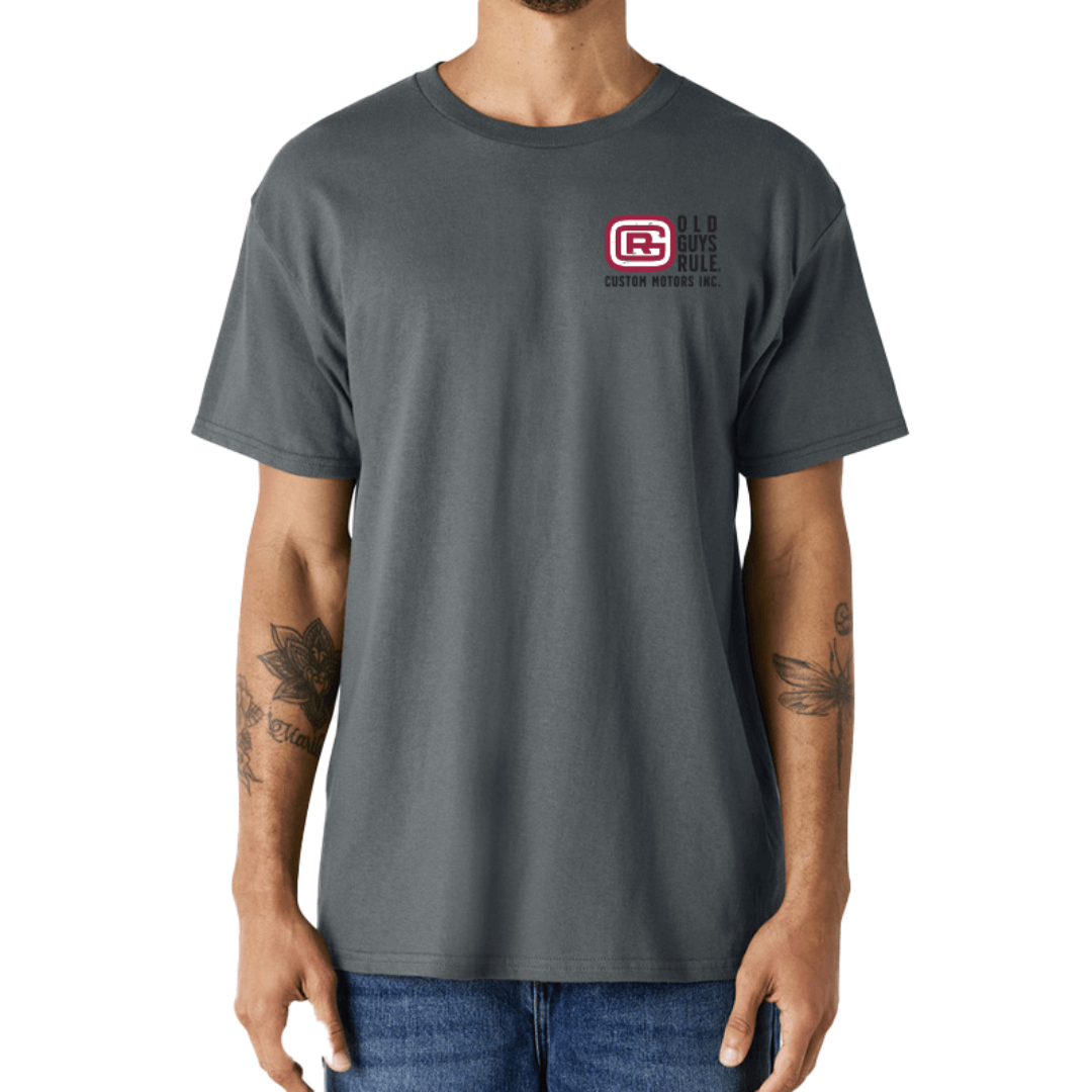 Stewart's Menswear, Mullumbimby. Photo shows model wearing Old Guys Garage T-shirt, front view. Colour is charcoal with black, red and white Old Guys Rule logo print on left chest.