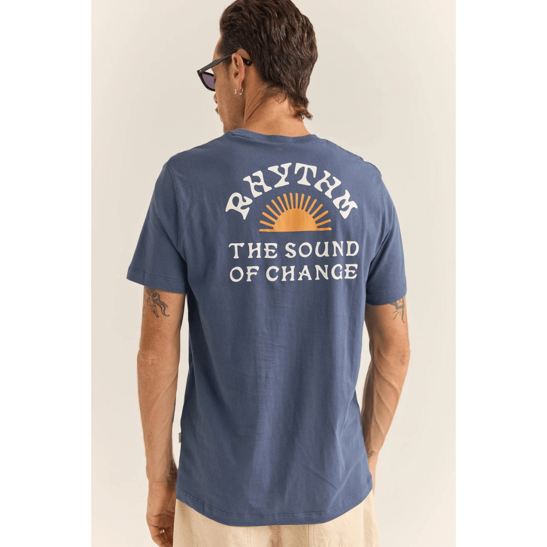 Stewarts Menswear, Mullumbimby. Rhythm Livin Awake Tee-shirt. Colour is blue. Photo shows model wearing Rhythm Awake T-shirt, back view. Rhythm logo with sun print and the words "The sound of change"