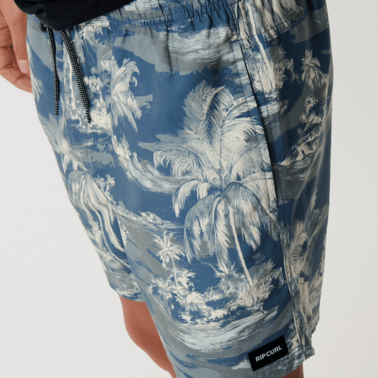 Stewarts Menswear Rip Curl Dreamers Volley Short. Colour is pine, a blue base with pine green island/palm tree print all over. Photo shows close up view of model wearing Rip Curl Dreamers Volley Short available at Stewarts Menswear, Mullumbimby