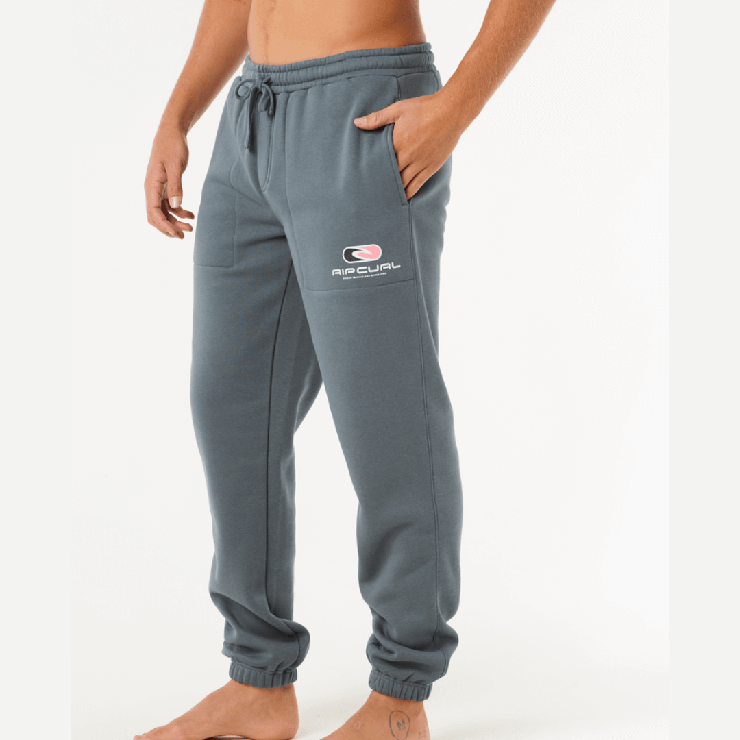 Stewart's Menswear, Mullumbimby. Rip Curl Icons of Surf Track pant. Photo shows model wearing Rip Curl Icons of Surf Track Pant, side view. Colour is Pine with side pockets and Rip Curl logo on leg. Elastic waist and elastic cuffs at ankles.
