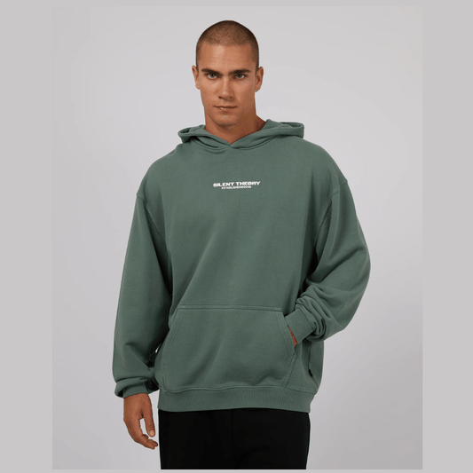 Front view of man wearing a green hoodie with a logo on a gray background. Silent Theory Essential Theory Hoodie with front and back logo print available at Stewart’s Menswear Mullumbimby.