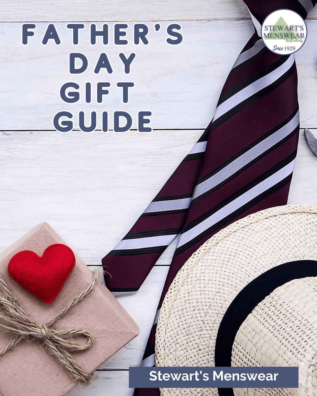 A Father's Day gift guide themed around men's accessories, featuring a burgundy and silver striped necktie, a cream straw hat, a small wrapped gift box with a red heart, and a red felt heart, all arranged on a white wood background. The text reads 'FATHER'S DAY GIFT GUIDE' and 'Stewart's Menswear'.
