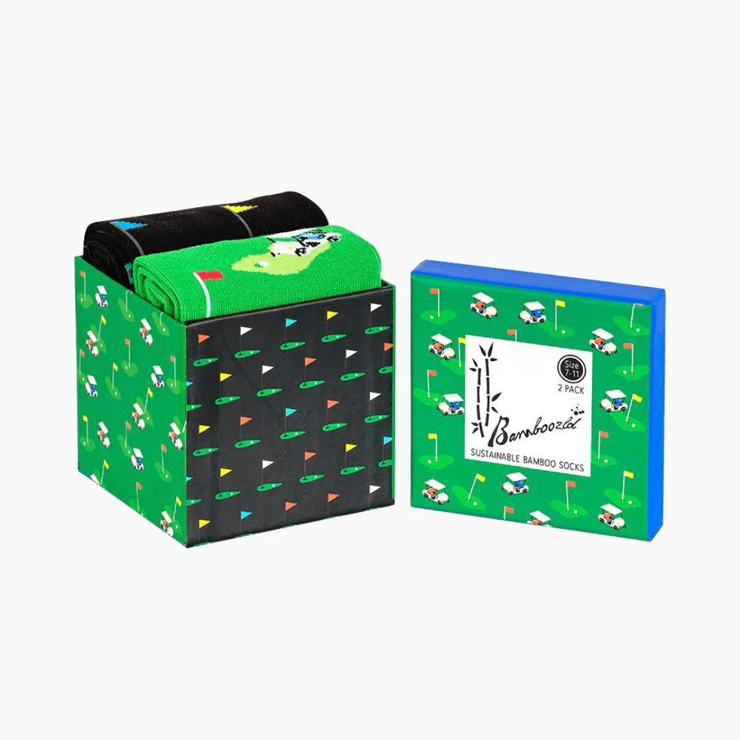 Stewarts Menswear Bamboozled socks 2 pack gift box. This Gift Box is the perfect gift, featuring two pairs of novelty crew socks packaged in a matching Gift Box.  Bamboozld Gift Boxes have a vibrant collection of quirky bamboo-blend socks which pack a playful punch. Theme is Golf. Includes one x black socks and one by green socks. Image is of box only featuring golf flag and golf buggy print all over.