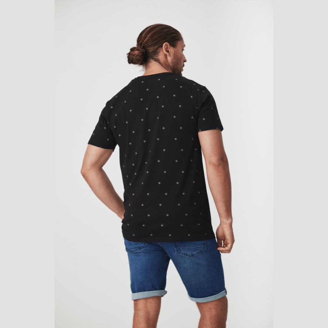 Stewarts Menswear Blackwood Apparel Arnold Henley neck tee-shirt. The Blackwood Apparel Arnold Short Sleeve Henley Tee is made from 100% cotton, combining classic comfort with modern durability. Colour is black with a tiny geometric printed all over. Chest pocket and contrast fabric in placket. Model wearing Arnold Henley tee with Perth Denim shorts, back view.