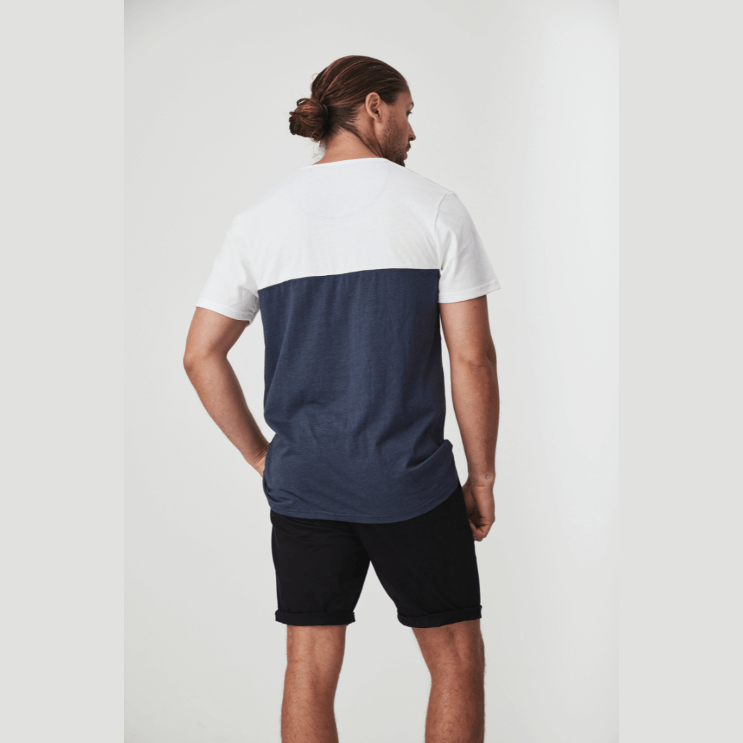 Stewart's Menswear Blackwood Apparel Bligh Henley Tee. The Blackwood Apparel Bligh Short Sleeve Henley Tee is made from a mix of 60% cotton and 40% polyester, combining classic comfort with modern durability. Colour block tee - body is Navy and sleeves/top chest is white. Front pocket is navy and contrast fabric in placket. Photo shows model wearing Bligh Henley Tee, back view.