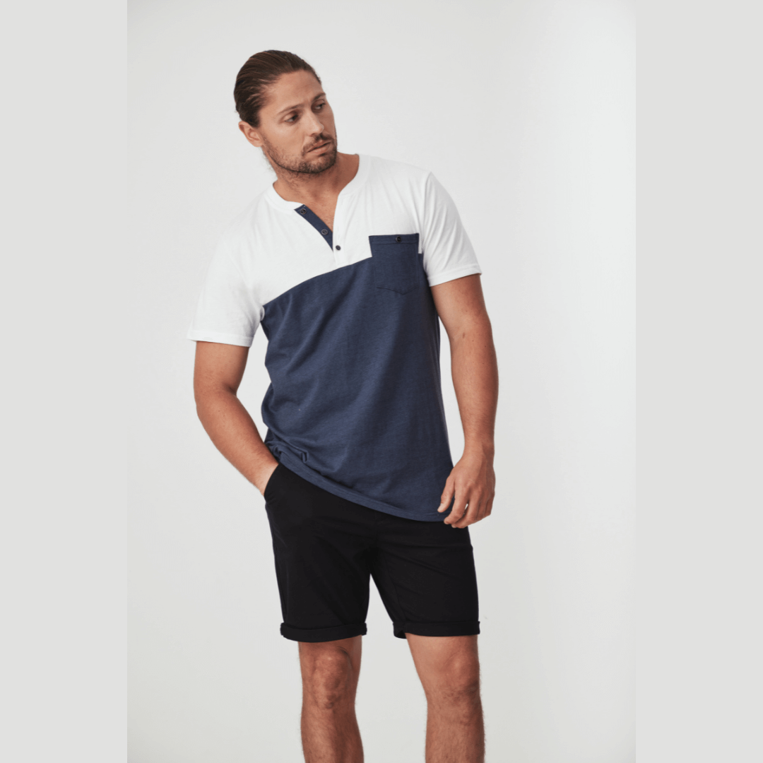 Stewart's Menswear Blackwood Apparel Bligh Henley Tee. The Blackwood Apparel Bligh Short Sleeve Henley Tee is made from a mix of 60% cotton and 40% polyester, combining classic comfort with modern durability. Colour block tee - body is Navy and sleeves/top chest is white. Front pocket is navy and contrast fabric in placket. Photo shows model wearing Bligh Henley Tee.