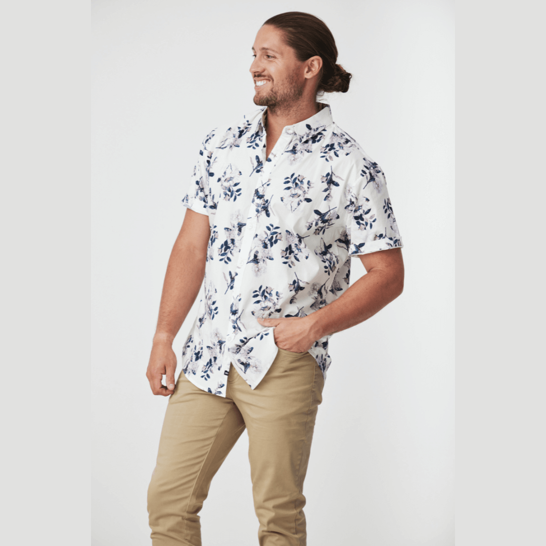 Stewarts Menswear Blackwood Apparel Cobar short sleeve shirt. The Blackwood Apparel Cobar Short Sleeve Shirt is made from a blend of 97% cotton and 3% elastane. This shirt offers both breathability and flexibility. White button through shirt with black/green/pale lilac floral print. Photo shows model wearing Cobar Short Sleeve shirt with chinos.
