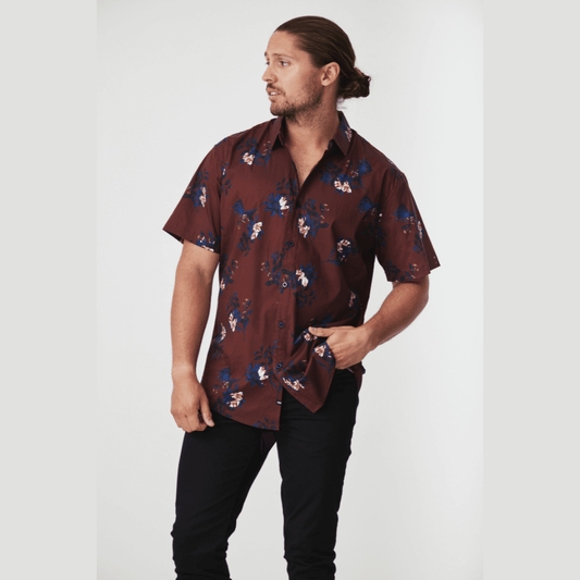 Stewarts Menswear Blackwood Apparel Scott Short Sleeve Shirt.The Blackwood Apparel Scott Short Sleeve Shirt is made from a blend of 97% cotton and 3% elastane. This shirt offers both breathability and flexibility. Rich burgundy coloured shirt with white and blue floral print all over. Photo shows model wearing Scott short sleeve shirt with black jeans. 