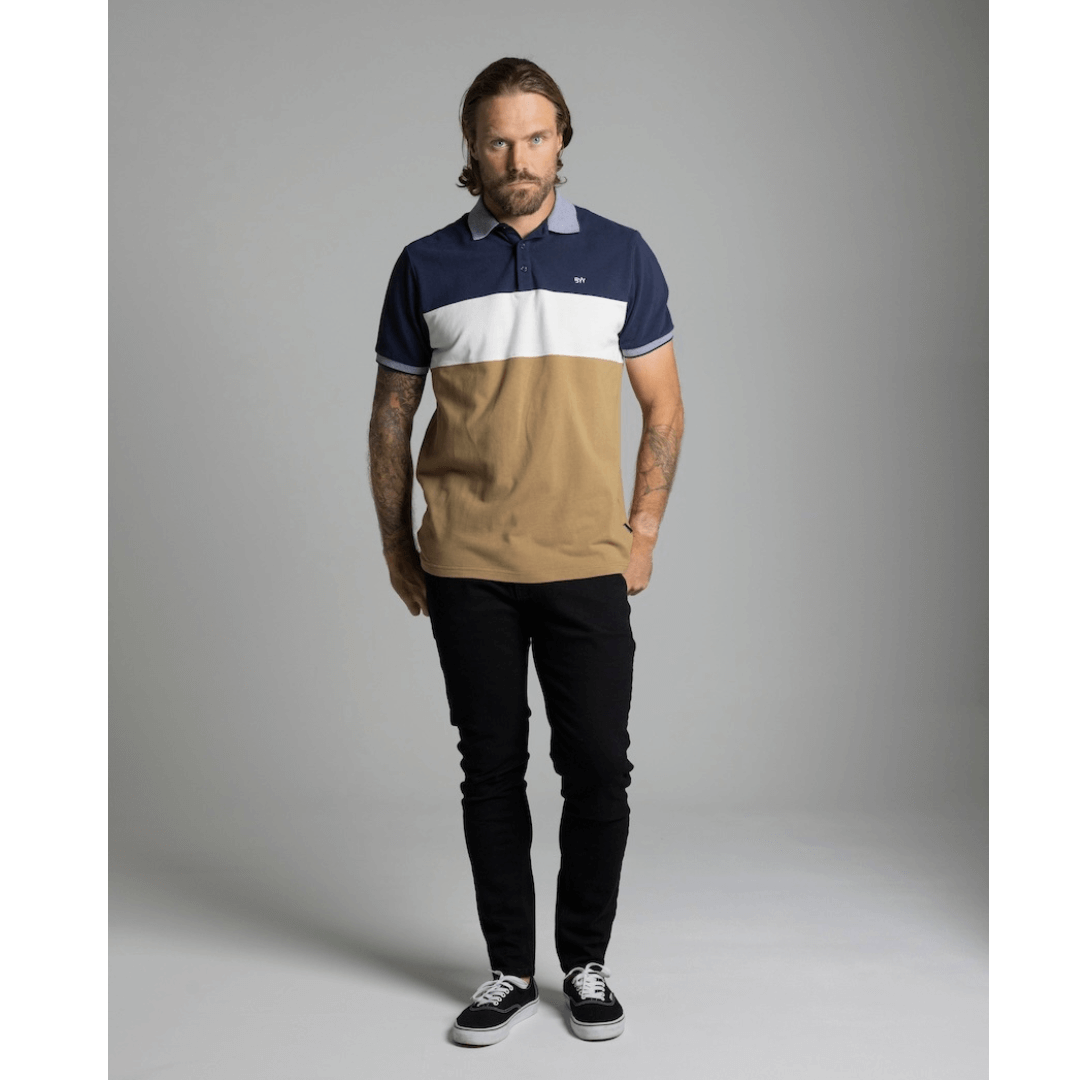 Stewart's Menswear Blackwood Apparel Waggs Lifestyle polo shirt. The Blackwood Apparel Waggs Lifestyle short sleeve polo is made from 100% cotton. Its colour block design in tobacco, navy and white gives it a casual sophistication. Photo shows model wearing Blackwood Waggs Polo Shirt front view.