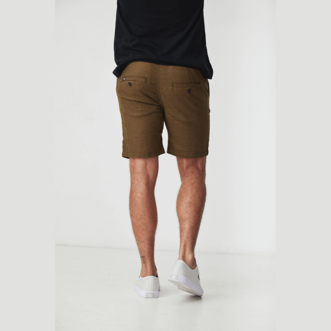 Stewarts Menswear Blackwood Apparel Ziggy linen shorts. made from a blend of 52% linen and 48% cotton. With an elastic waist and drawcord for a personalised fit. Photo shows model wearing Ziggy linen shorts with a black t-shirt. Colour is Khaki, back view.