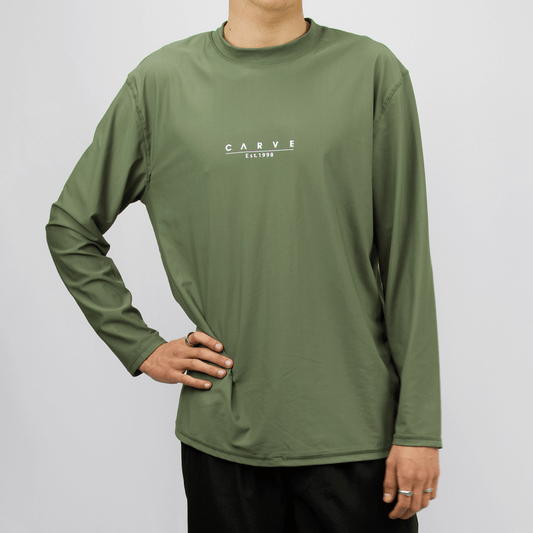 Carve Men’s Long Sleeve Swim Rashie. Relaxed-fit rash vest with UPF 50+ sun protection, available at Stewart’s Menswear Mullumbimby. Colour is khaki with small Carve print on front chest
