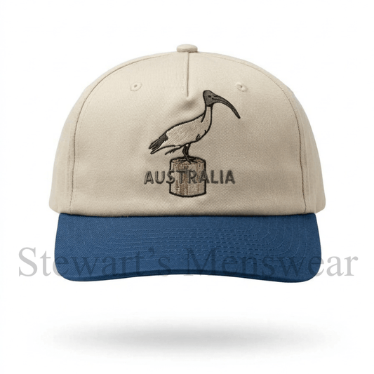 Bin Chicken Cap in stone with a blue brim, a 6-panel cotton cap with an embroidered ibis on a timber post and Australia lettering, available at Stewart’s Menswear Mullumbimby.