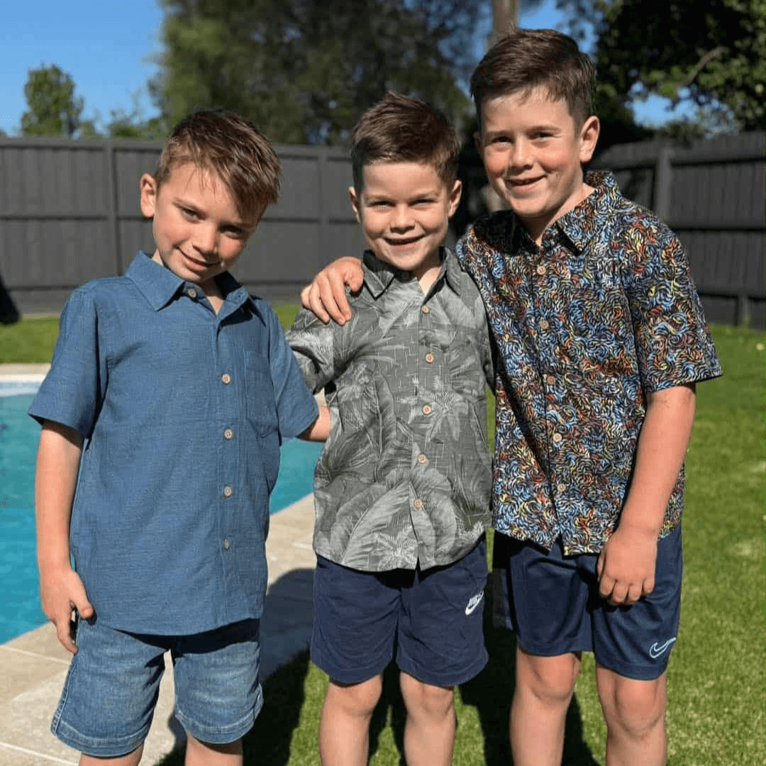 Three boys wearing Kingston Grange Bamboo shirts standing together by a pool with greenery in the background