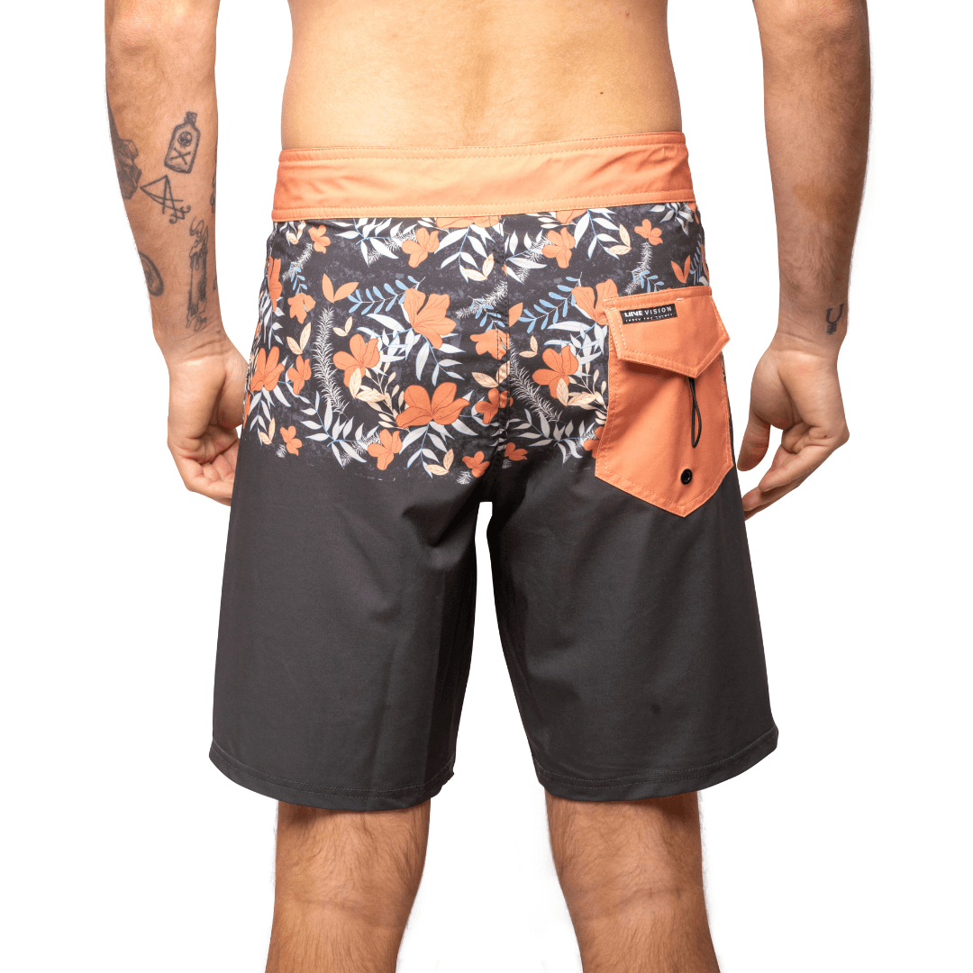 Stewarts Menswear Liive Vision Apparel Duo boardshort. Fitted waist with drawcord, back patch pocket with velcro closure and key loop in the back pocket. Orange waistband with orange/white/charcoal floral print block at top of shorts. Bottom of shirts is solid charcoal colour. Pocket at back is Orange. Back View.