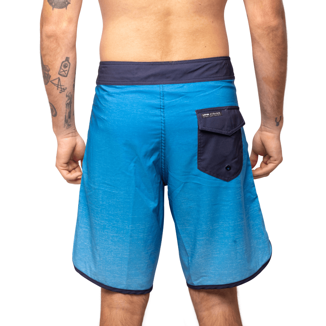 Stewarts Menswear Liive Vision Apparel Vague Boardshort. Trendy gradient colour design.   Fitted waist with drawcord, back patch pocket with velcro closure and keep loop in the back pocket. Dark blue waistband with gradient blue body. Scalloped leg with navy piping and Navy pocket on back.  Back View.