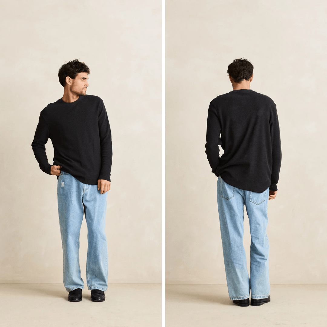 A man modeling a black long-sleeve crewneck sweater with light blue jeans, shown in a front-facing and back-facing side-by-side studio pose against a warm beige background.