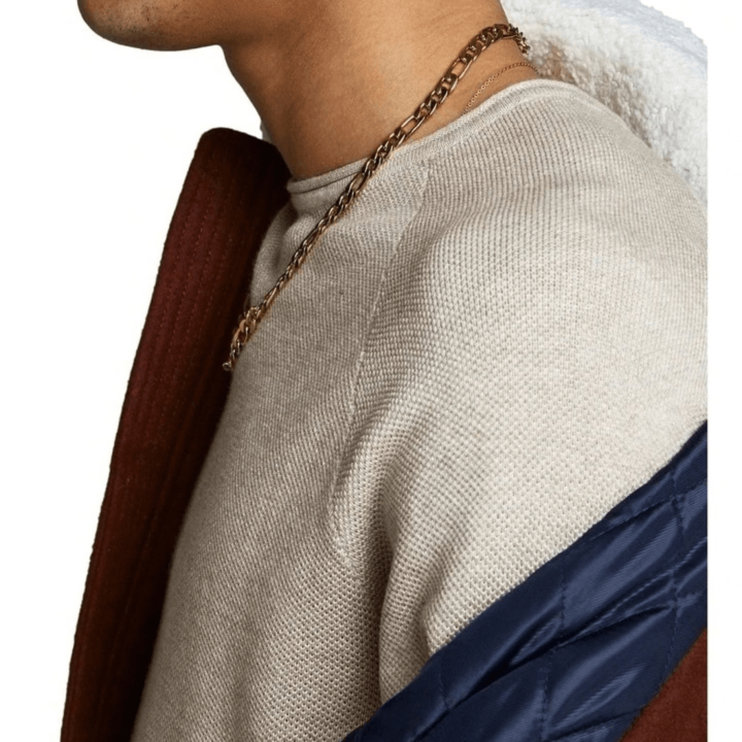 Close-up of a person wearing a beige sweater with a gold chain necklace, white shirt, and brown jacket. Jack & Jones Hill cotton knit crew neck pullover in black available from Stewart's Menswear in Mullumbimby.