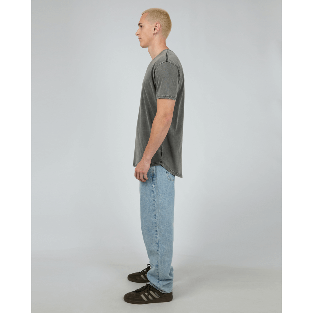 Man wearing Silent Theory Tail Tee available from Stewart's Menswear in Mullumbimby. Pigment washed scooped tail at back, charcoal colour, side view.