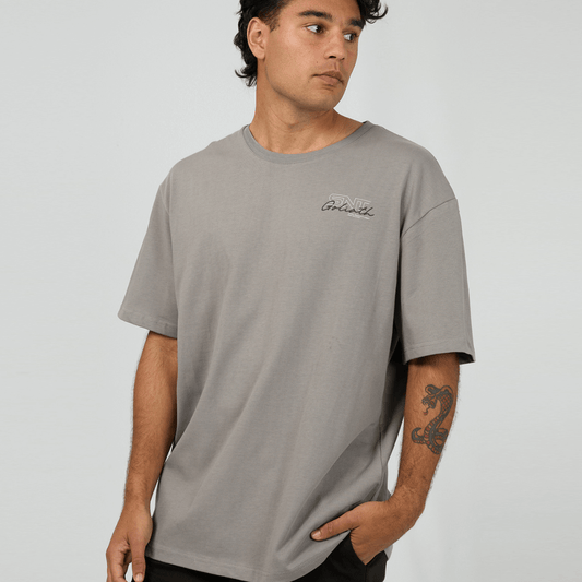 Stewart's Menswear mullumbimby. St Goliath Link Script Tee. Photo shows front view of model wearing St Goliath Link Script Tee, Smoke (light grey) colour with small logo on left chest.