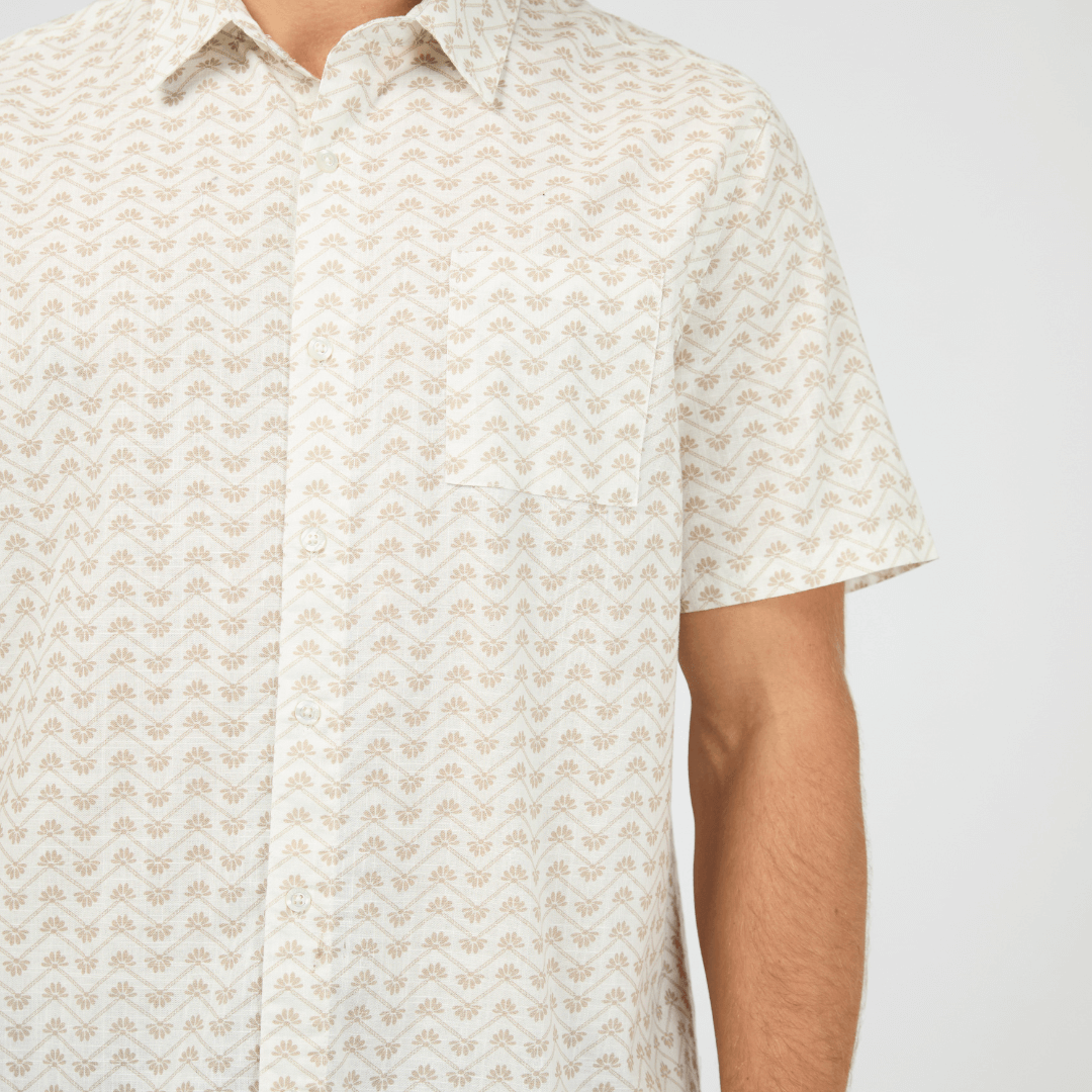 Close up view of model wearing St Goliath Lotus Short Sleeve Shirt available at Stewart’s Menswear Mullumbimby. Men’s relaxed-fit cotton short sleeve shirt with collared neckline and button-down design. White shirt with small tan coloured lotus print all over.