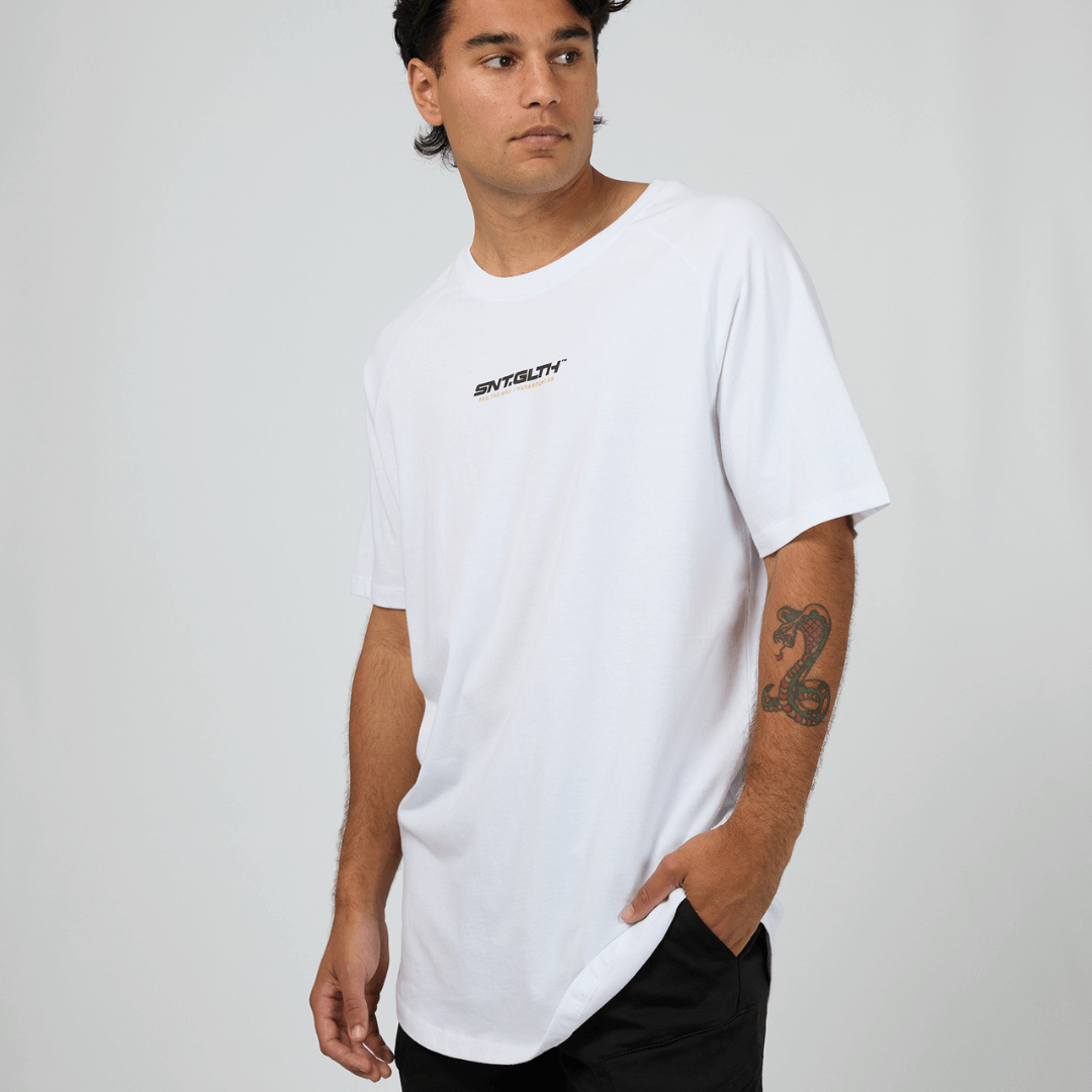 Stewarts Menswear, Mullumbimby. Photo shows model wearing St Goliath Pace Raglan Tee, front view. Colour is white with black and Gold foil print across chest.