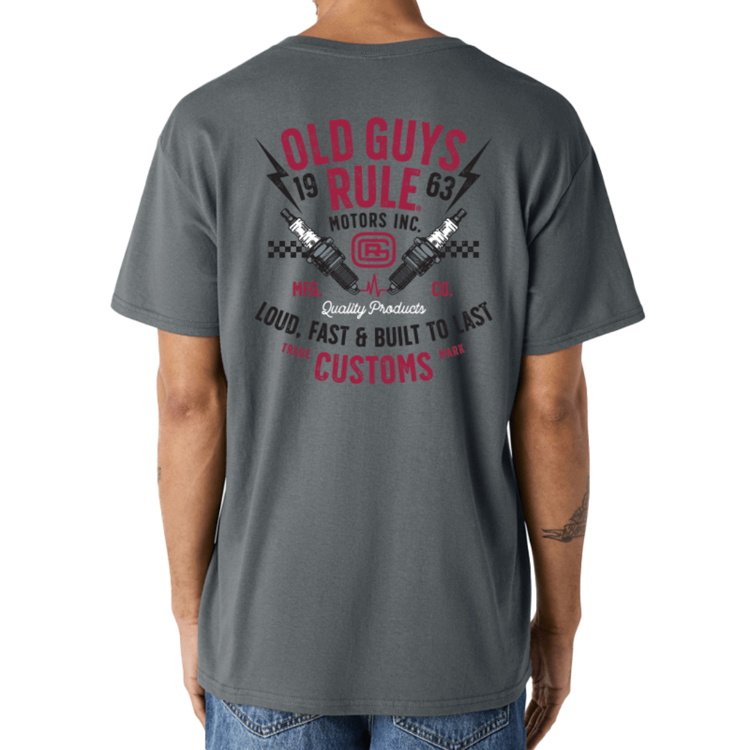 Stewart's Menswear, Mullumbimby. Photo shows model wearing Old Guys Garage T-shirt, back view. Colour is charcoal with black, red and white larg print on back: Old Guys Rule Motors Inc. Loud, fast and built to last.