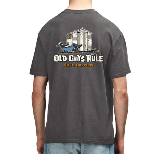 A man wearing a dark gray t-shirt, viewed from the back. The shirt features a graphic of a white shed with a man resting in front of it, with the text 'OLD GUYS RULE' and 'SHED HAPPENS' printed below.
