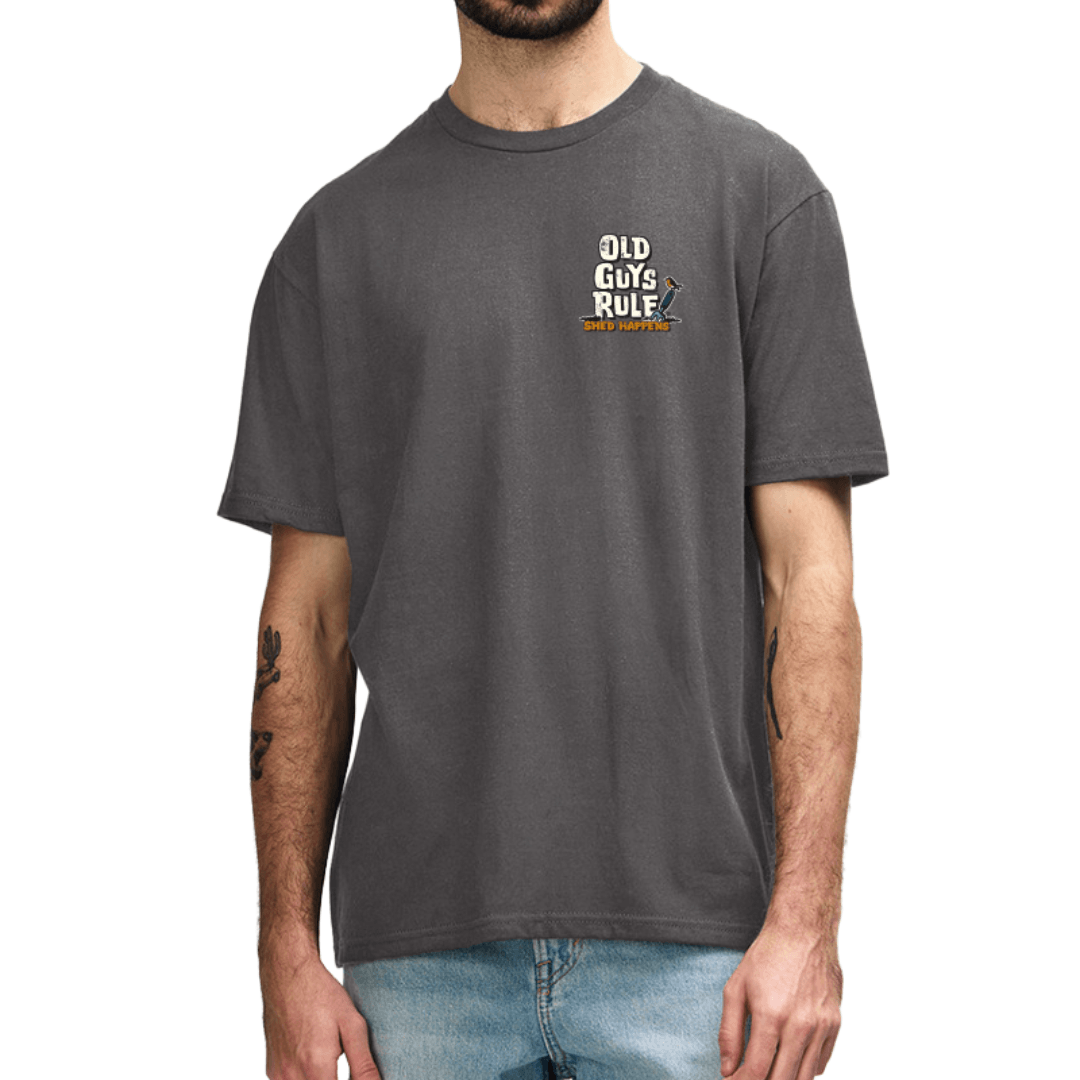 A man wearing a charcoal coloured t-shirt with a small graphic on the left chest that reads 'OLD GUY RULE' with gardening fork, paired with blue jeans against a plain white background.