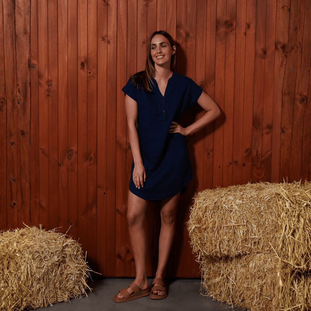 Lifestyle photo of female model wearing Ritemate Pilbara Alina Cap Sleeved Linen Dress in Navy, 100% linen dress with side pockets available at Stewart's Menswear Mullumbimby.