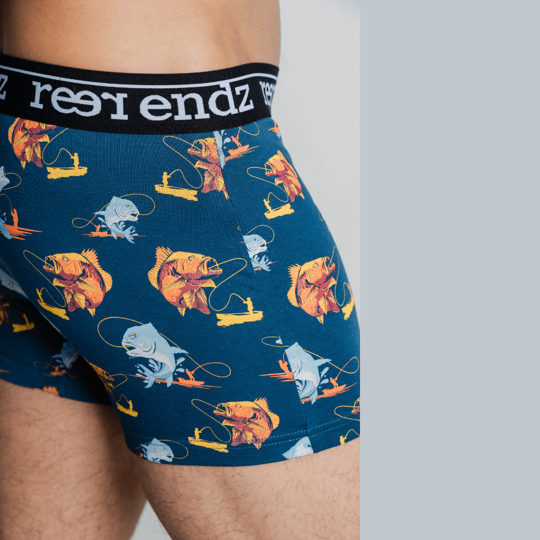 Stewarts Menswear Reer endz organic Cotton underwear. Hooked is a rich blue coloured men's trunk with a man in a fishing boat catching a fish printed all over. Photo is a close up of model wearing Hooked men's underwear.