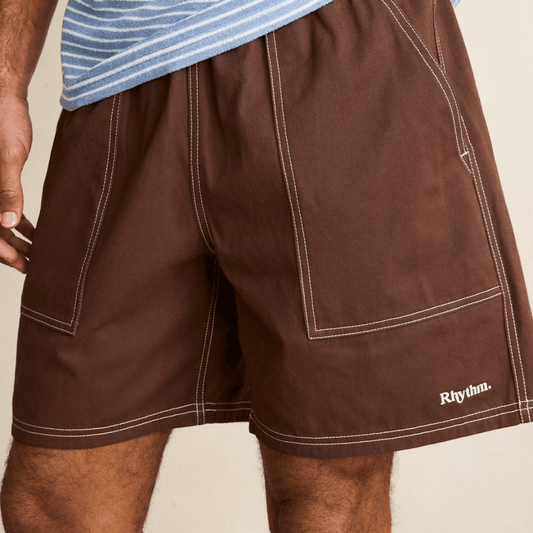 Close-up of a man wearing Rhythm Contrast Stitch Jam shorts in chocolate brown with white contrast stitching.