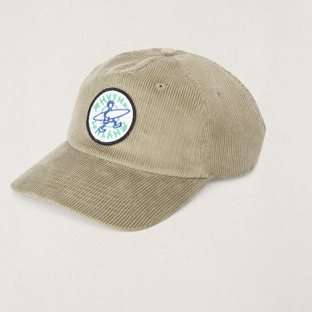 A stone coloured corduroy baseball cap with a circular embroidered patch on the front featuring a blue and green surfer graphic. Rhythm Jaunt Cord cap available from Stewart's Menswear in Mullumbimby