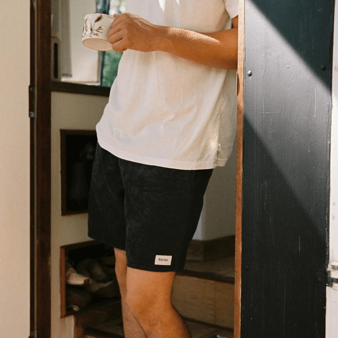 Stewarts Menswear Rhythm classic cord jam. Shorter length, elastic waist with drawcord. Rhythm labels on back and front. Colour is Black. Photo shows model wearing an outfit featuring black coloured classic cord jam shorts.