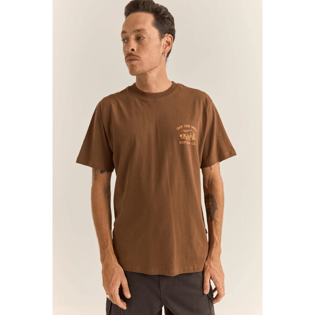 Stewarts Menswear Rhythm Livin Worn Path Tee. A signature print of cacti with celebrates life "Off The Well". Photo shows model wearing Worn Path tee front view with small print on left chest. Colour is Chocolate (vintage wash).