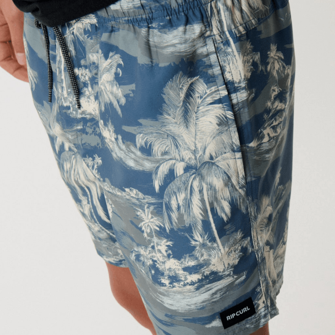Stewarts Menswear Rip Curl Dreamers Volley Short. Colour is pine, a blue base with pine green island/palm tree print all over. Photo shows close up view of model wearing Rip Curl Dreamers Volley Short available at Stewarts Menswear, Mullumbimby