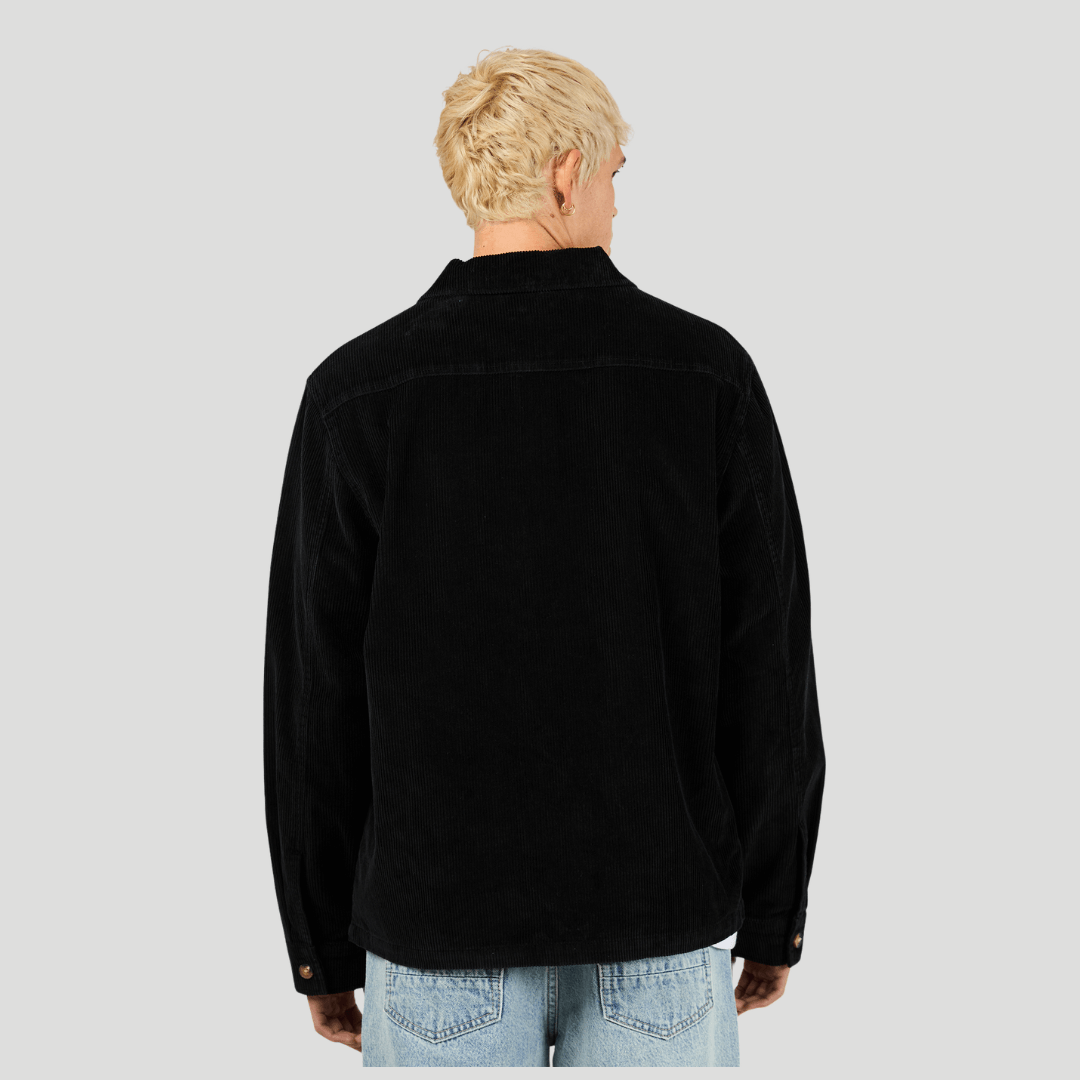 Back view of man wearing a black corduroy shirt and light blue jeans on a gray background. Silent Theory Jameson Cord Shirt in cotton corduroy available at Stewart’s Menswear Mullumbimby.
