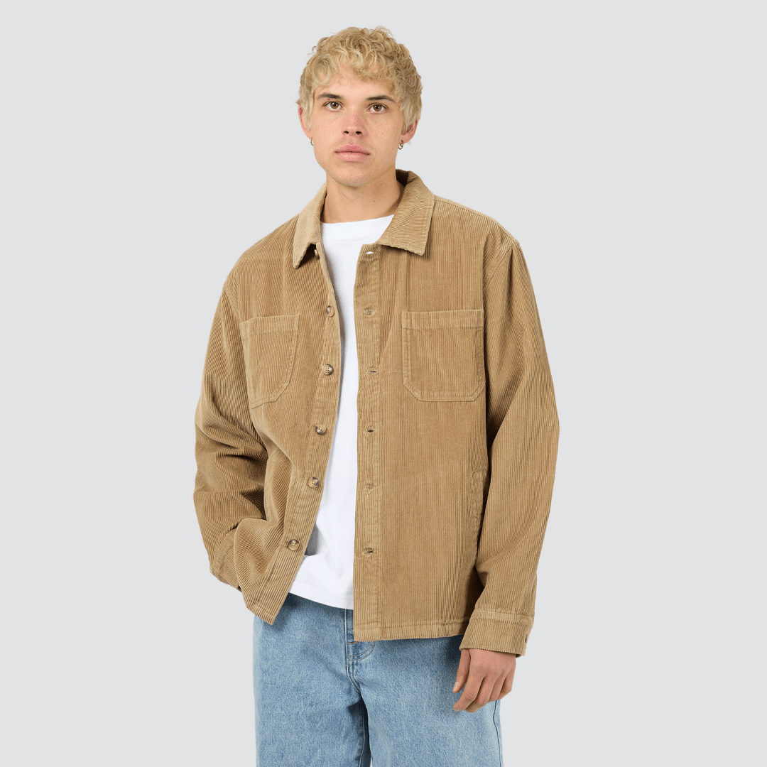 Front view of man wearing a tan coloured corduroy shirt and light blue jeans on a gray background. Silent Theory Jameson Cord Shirt in cotton corduroy available at Stewart’s Menswear Mullumbimby.