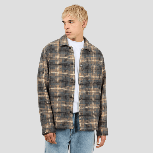 Model wearing a plaid shirt over a white tee-shirt. Silent Theory Stature Overshirt Brown in classic check with chest pockets, available at Stewart’s Menswear Mullumbimby.