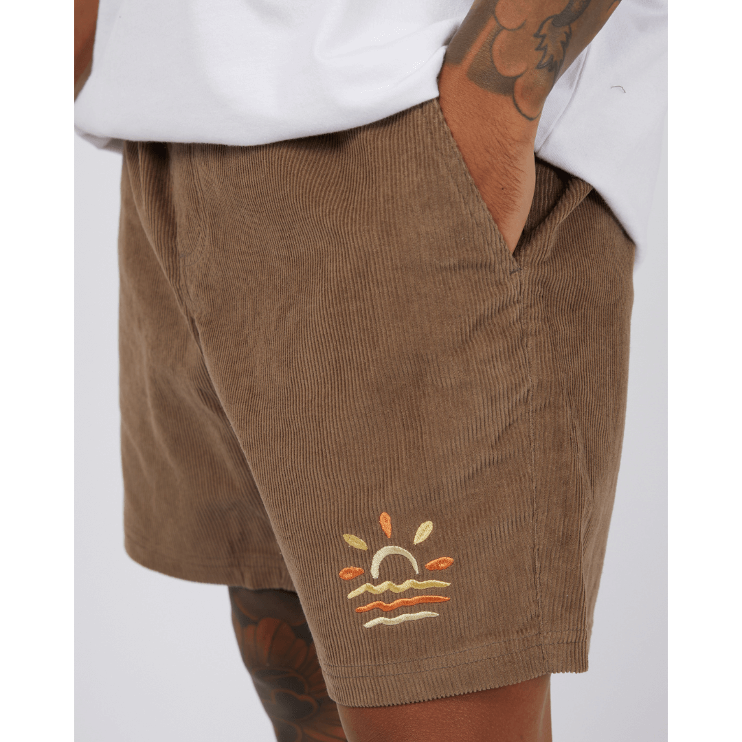 Stewarts Menswear St Goliath Wind Down Cord Short. Photo shows close up view of model wearing St Goliath Wind Down Cord short. Colour is brown with a yellow and orange sun/ocean logo embroidered on front.