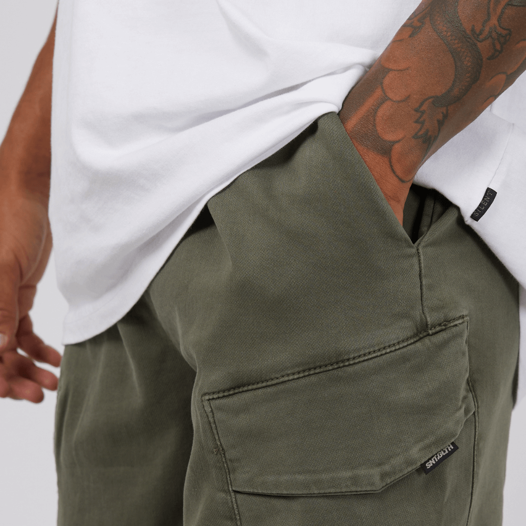 Stewarts Menswear St Goliath Gully Cargo shorts. The inset cargo pockets, waist band, and side pockets make these hybrid denim shorts a must-have for any adventure. Photo shows close up view of model wearing St Goliath Gully Cargo Short. Colour is Khaki